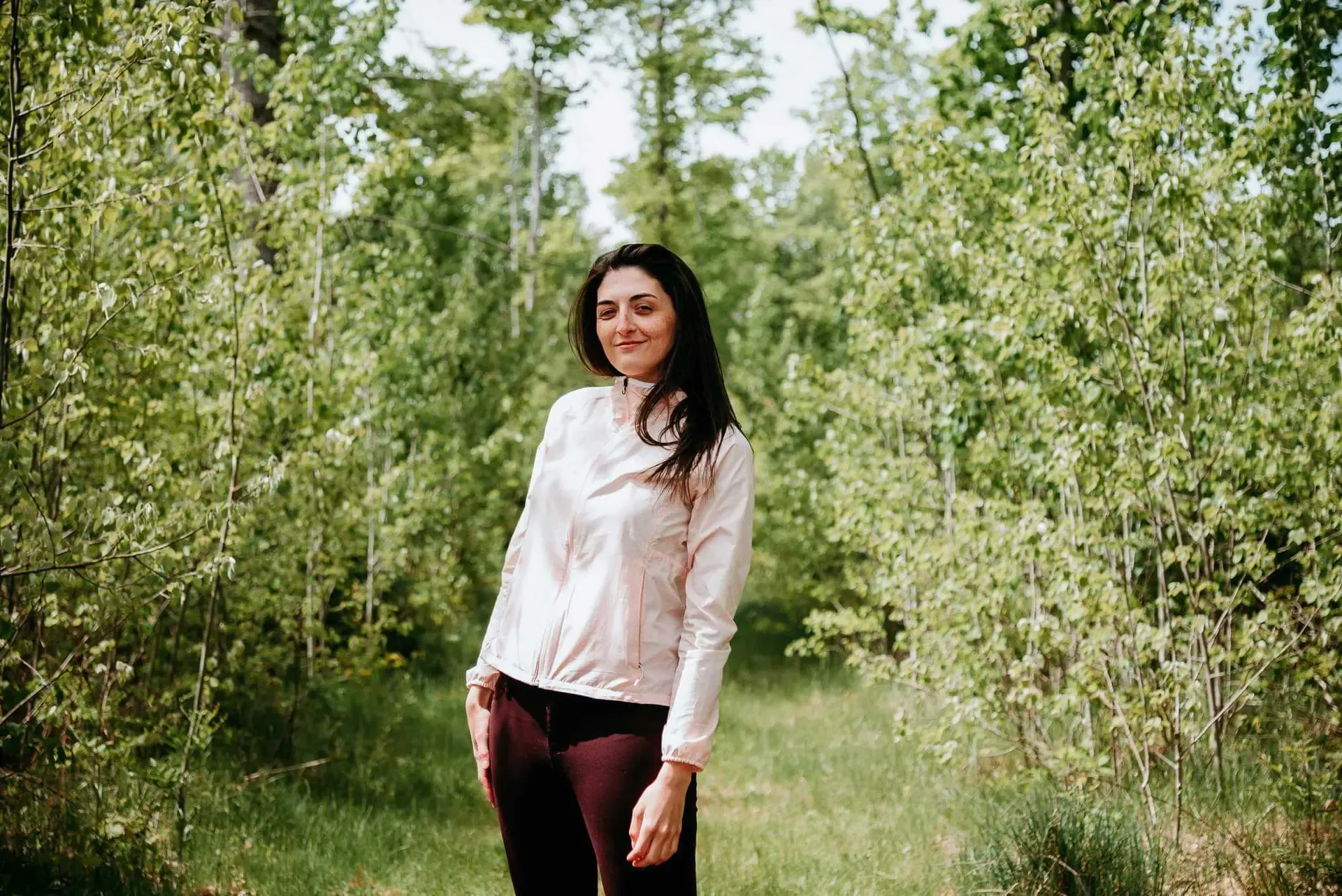 Brittany VanderWall stands on a grassy path running through a young forest.