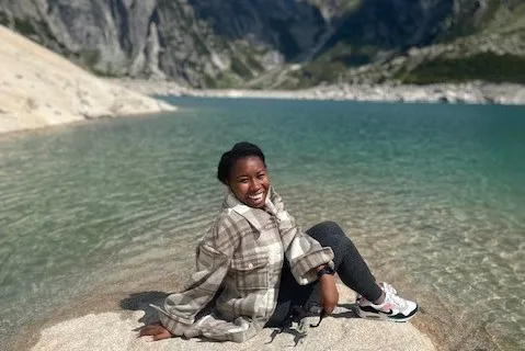 Jasmine Brown sitting on a rocky outcropping over a mountainous pond.