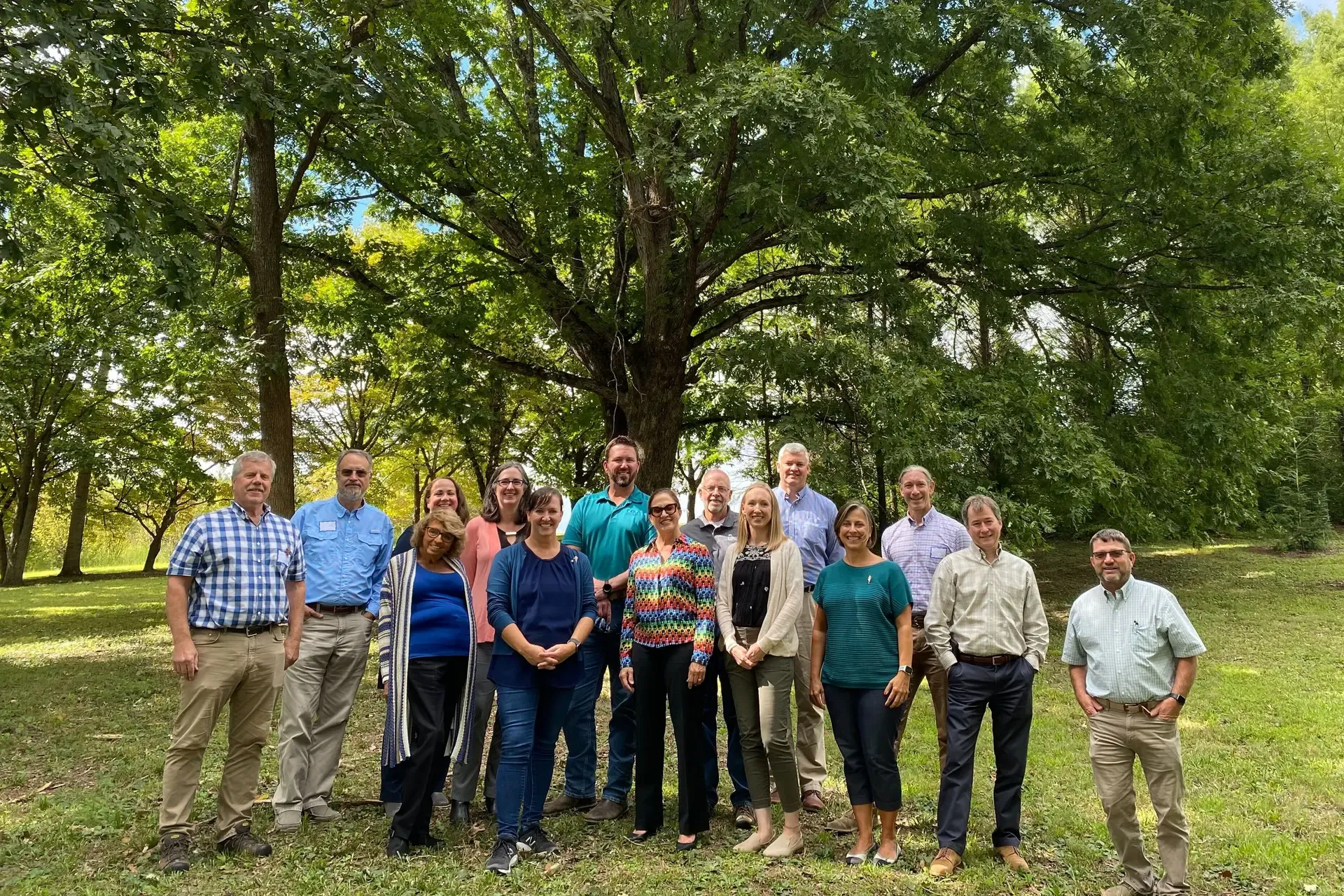 A group of people standing outside and posing for a group photo in front of a large oak tree.